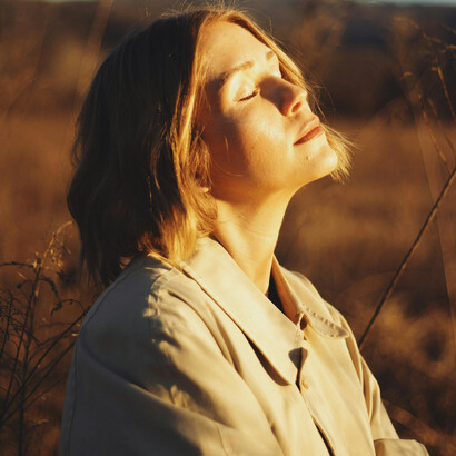 A tranquil autumn sunset in Brevard, North Carolina, a woman standing in a sunlit field, bathed in warm golden light, US