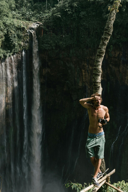 On the edge of a waterfall cliff, a man photographs the view, reflecting the courage to step beyond comfort