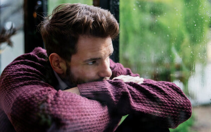 A heartbroken man, looking through the window on a rainy day, waiting for his lover to come back home