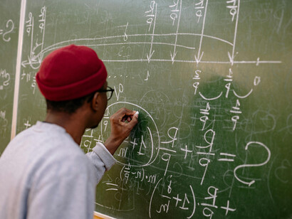 A student seen from behind solving a quantum mechanics problem on a chalkboard