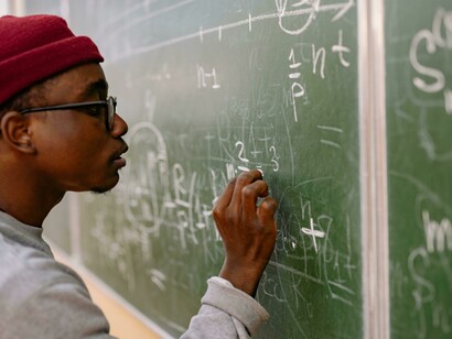 From behind, a student concentrates on solving a complex quantum mechanics problem at the board
