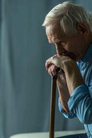 Un uomo si appoggia al proprio bastone pensieroso