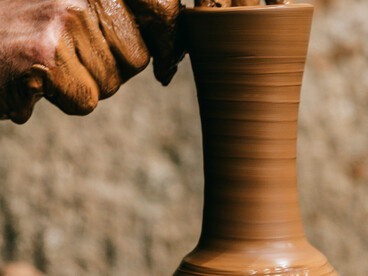 Man forming a clay vase in a bright artist studio with natural light, surrounded by craft supplies on the desk