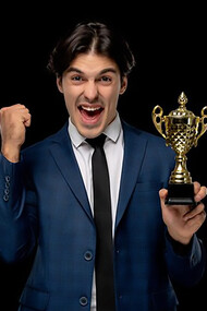 Successful young businessman in a dark blue suit and tie, holding a trophy with excitement