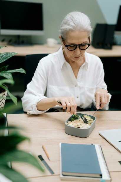 An elderly woman enjoys a packed lunch at the office, highlighting healthy eating habits for healthy aging
