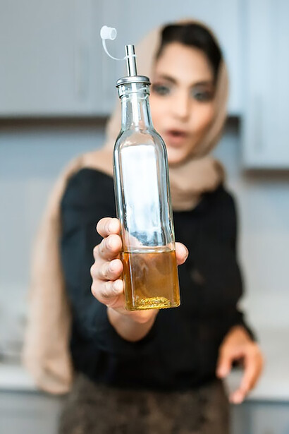 A health-conscious woman, holding a bottle of olive oil, is preparing to cook