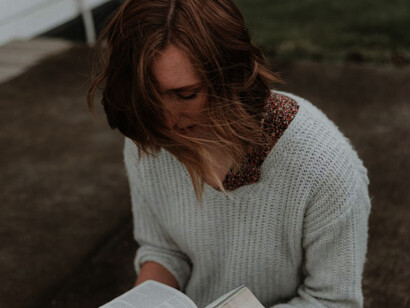 Sitting on the gray concrete pavement, a woman holds her Bible, absorbed in its words, as she enjoys a peaceful pause