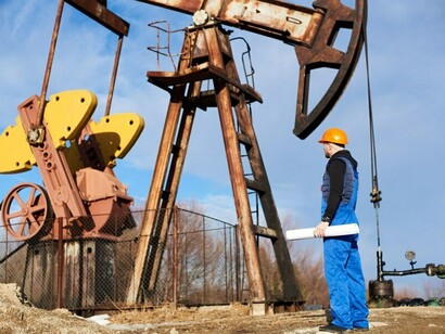 A pump jack in motion with engineers monitoring the oil field under a clear, sunny sky