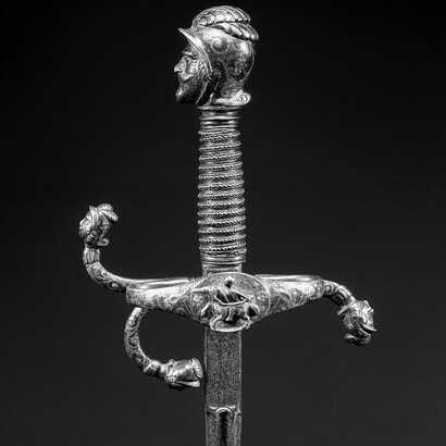Rapier, dated 1595, crafted from russeted and gilded steel with inlaid silver, featuring a pommel and quillon terminals chiseled in the form of warrior heads