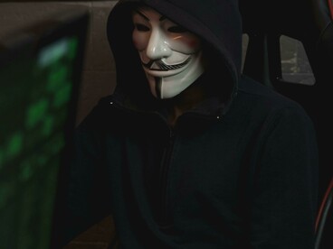 A hooded figure at a computer represents disinformation and sabotage in cyberspace
