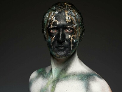 A person with layered paint across their face, representing the emotional depth and complexity modern masculinity is capable of 