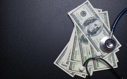 A stethoscope lying on currency bills, representing how the healthcare industry is often driven by profit and financial incentives rather than patient care