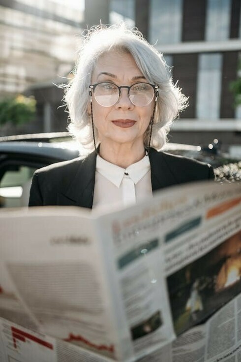An elderly woman sitting on the street, reading a newspaper, embodying the essence of French media culture