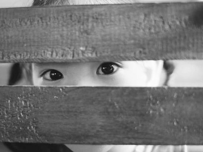 The empty gaze of a child framed by a weathered wooden structure