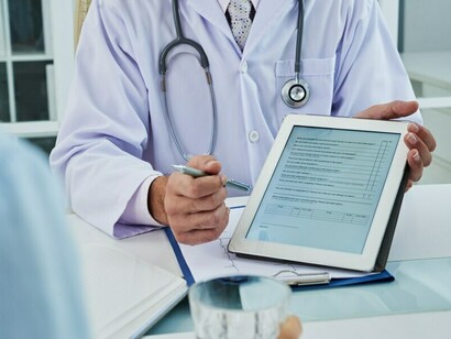 A doctor reviewing medical records on a digital tablet to track and guide the patient's health progress