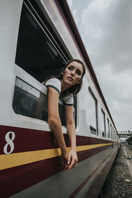 A woman’s head and hands are visible outside a train window under a cloudy daytime sky