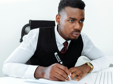 A Black man sitting at his office desk, looking depressed and stressed