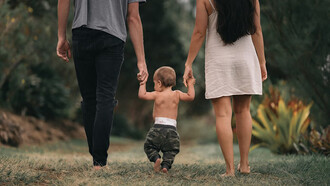 A couple walks barefoot through the garden, holding hands with their child