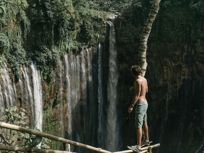 A man takes a photo from a cliffside near a waterfall, embodying the leap from safety to freedom