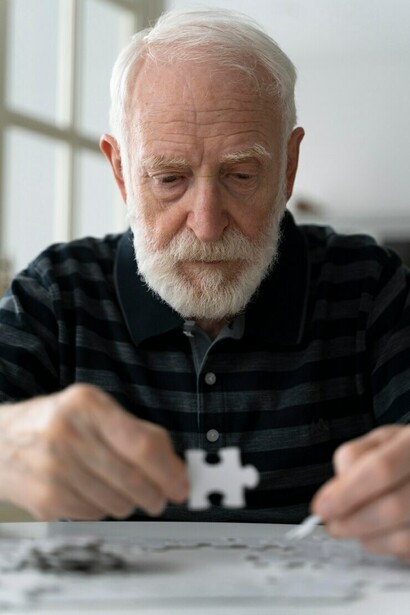 An elderly man living with Alzheimer’s focuses on completing a puzzle at the table