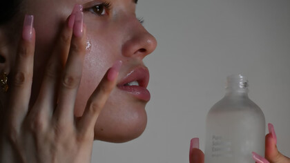 A person holding a skincare bottle, preparing to apply a beauty product