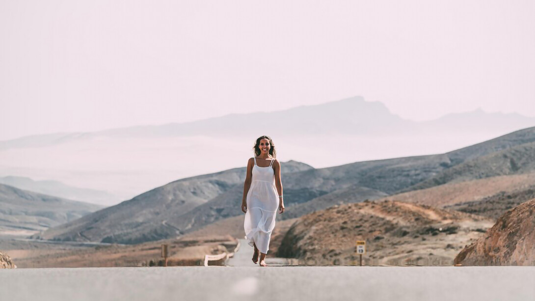 A woman walking on a road near hills under a cloudy sky, smiling, symbolizing her healing journey, spiritual warfare, and overcoming trauma, embodying peace and purpose