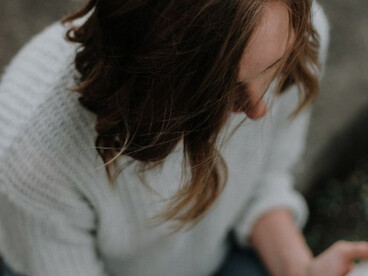 A woman sits on the gray concrete pavement, holding and reading her Bible in a moment of reflection