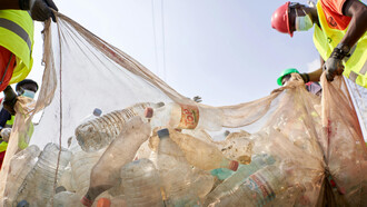 A low-angle photograph captures people carrying a garbage bag full of plastic bottles
