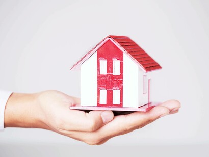 Una mano tiene in palmo un modellino di casa con tetto rosso e pareti bianche