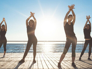 At sunrise, sportive women dancing Zumba by the sea demonstrate how physical activity enhances mental health