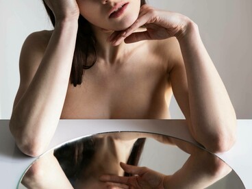 Primo piano di donna con gli occhi socchiusi, il cui viso è riflesso capovolto in uno specchio circolare