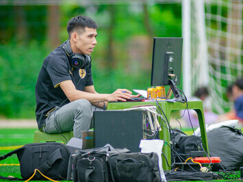 A man operating a portable computer on the sports field, with the director of football and manager observing
