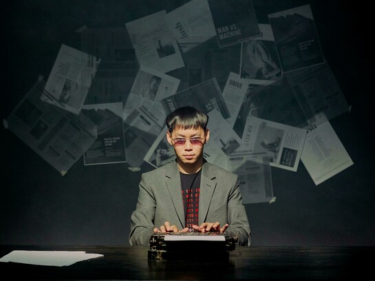 A journalist at a typewriter, staring at the camera as scattered newspapers fly behind him, symbolizing the chaos of the news cycle
