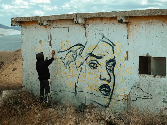 An expressive artist spray-painting the wall of an abandoned building, embodying the spirit of a creative soul
