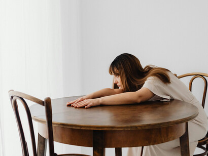 A woman leaning on a table, quiet grief marked by an empty chair