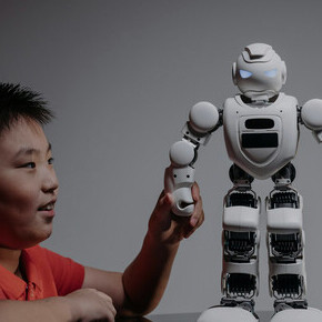 A boy stares at a white toy robot as if meeting a new friend from the future