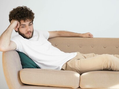 Uomo sul divano con l'aria stanca e assente: "In questo stato di *afterburn* (calo neurochimico) il cervello sovrastima gli aspetti negativi della situazione e sottostima le risorse future e le tue capacità di far fronte a contesti e situazioni stressanti"