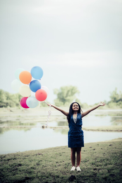 In the serenity of nature, a young woman holds colorful balloons, embodying self-care, relaxation, and the peaceful warmth of sunlight on her skin