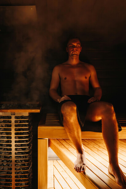 Immersed in the warmth of a modern Nordic sauna, a man embraces heat therapy to enhance physical resilience, vitality, and longevity