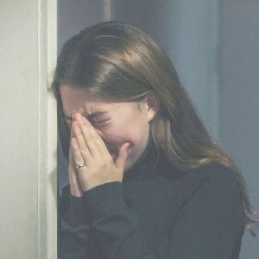 A woman leans against the wall, tears streaming down her face