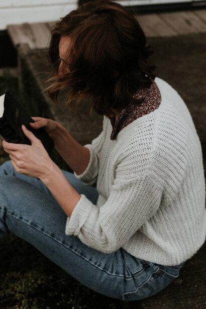 A woman sits on the gray concrete pavement, deeply engrossed in reading her Bible, finding peace in the quiet moment