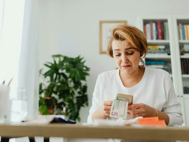 A woman sits at home counting money while paying bills, showing the emotional strain of financial hardship