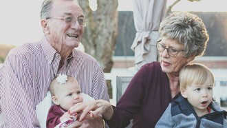 An elderly grandmother and grandfather lovingly hold their grandchild on their lap