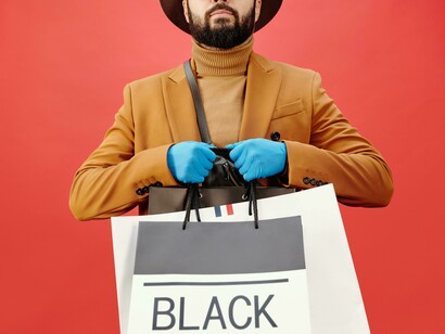 A man in a brown blazer carrying shopping bags while using his cell phone, illustrating the link between digital connectivity, consumer habits, and the pursuit of social belonging