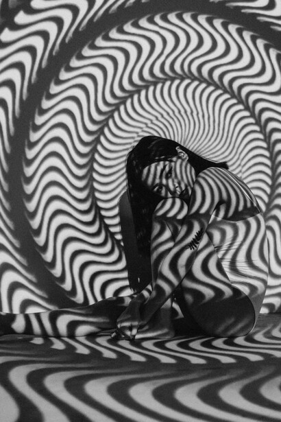 A woman rests beside a black and white striped wall, her stillness forming a silhouette of thought—inviting notions of inner light, contemplation, and the architecture of ideas