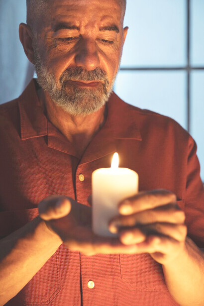 A senior man praying in church, holding a candle as a symbol of his spiritual struggle and path to redemption through faith