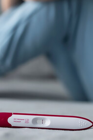 A woman sitting on the floor, appearing invisible and distressed behind a negative pregnancy test, reflecting the emotional impact of infertility