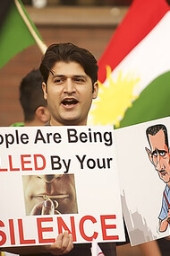 A man participating in the Syrian protests holds a sign that reads: "People are being killed by your silence"