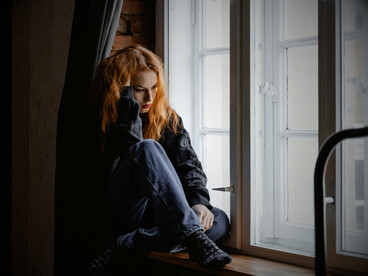 A solitary woman sitting next to the windows, surrounded by nothing but her thoughts