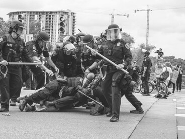Police officers encircle a man lying on the ground, highlighting the imbalance of power